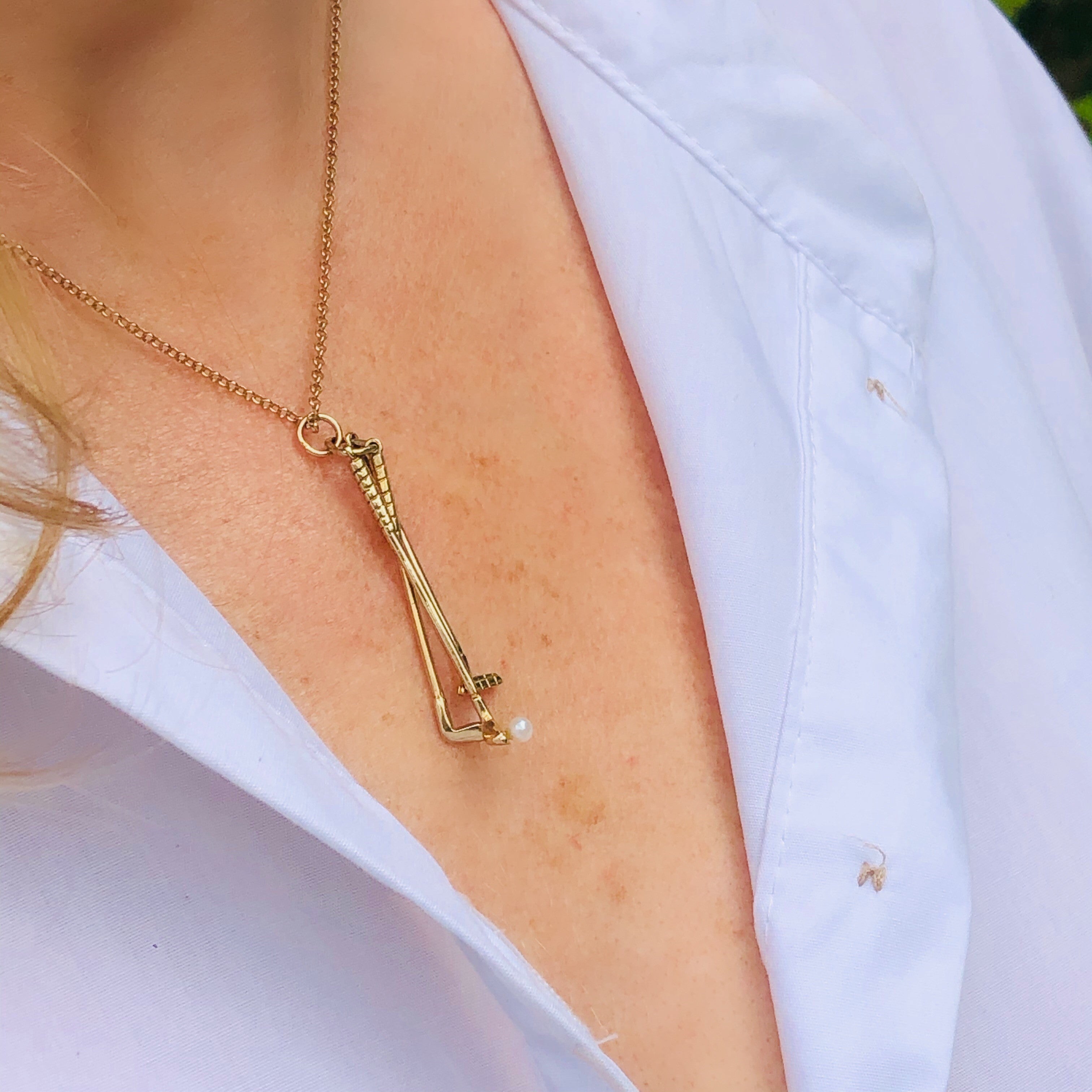 1973 Gold & Pearl Golf Clubs Necklace photographed on a model wearing a white shirt