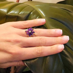 Vintage Amethyst and Diamond Flower Ring worn on models ring finger with a large leaf in the background