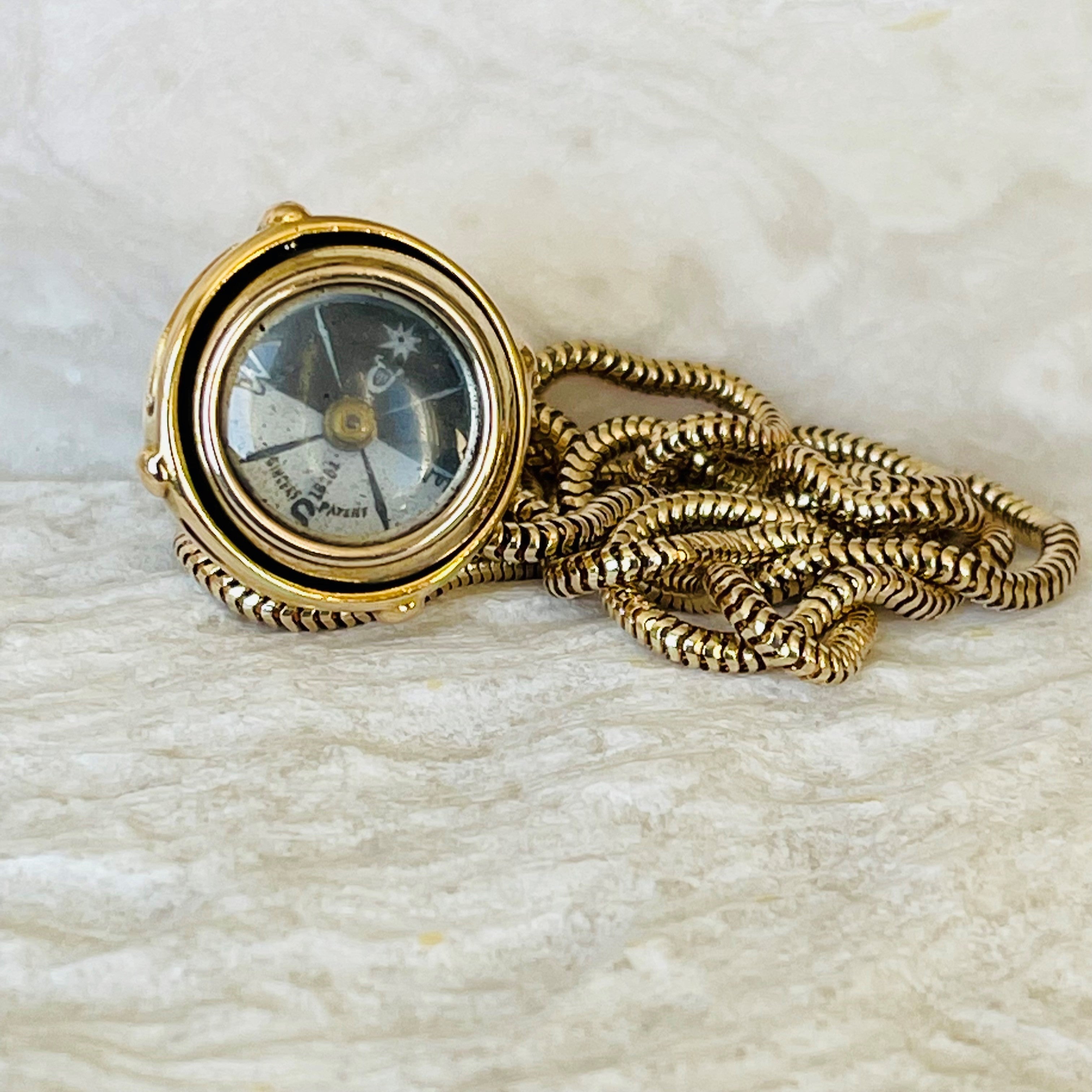 Antique Articulated Gold Gimbal Orb Compass Pendant on a gold chain photographed on a light cream marble background 