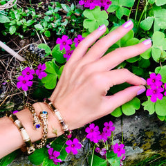 Alluring Amethyst & Topaz Torque Bangle photographed with other bangles on a models wrist with purple flowers and green leaves in the background