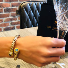 Alluring Amethyst & Topaz Torque Bangle photographed on a models wrist. Model is holding a crystal wine glass, with a brick wall, table, black chair and baroque rocks bag in the background