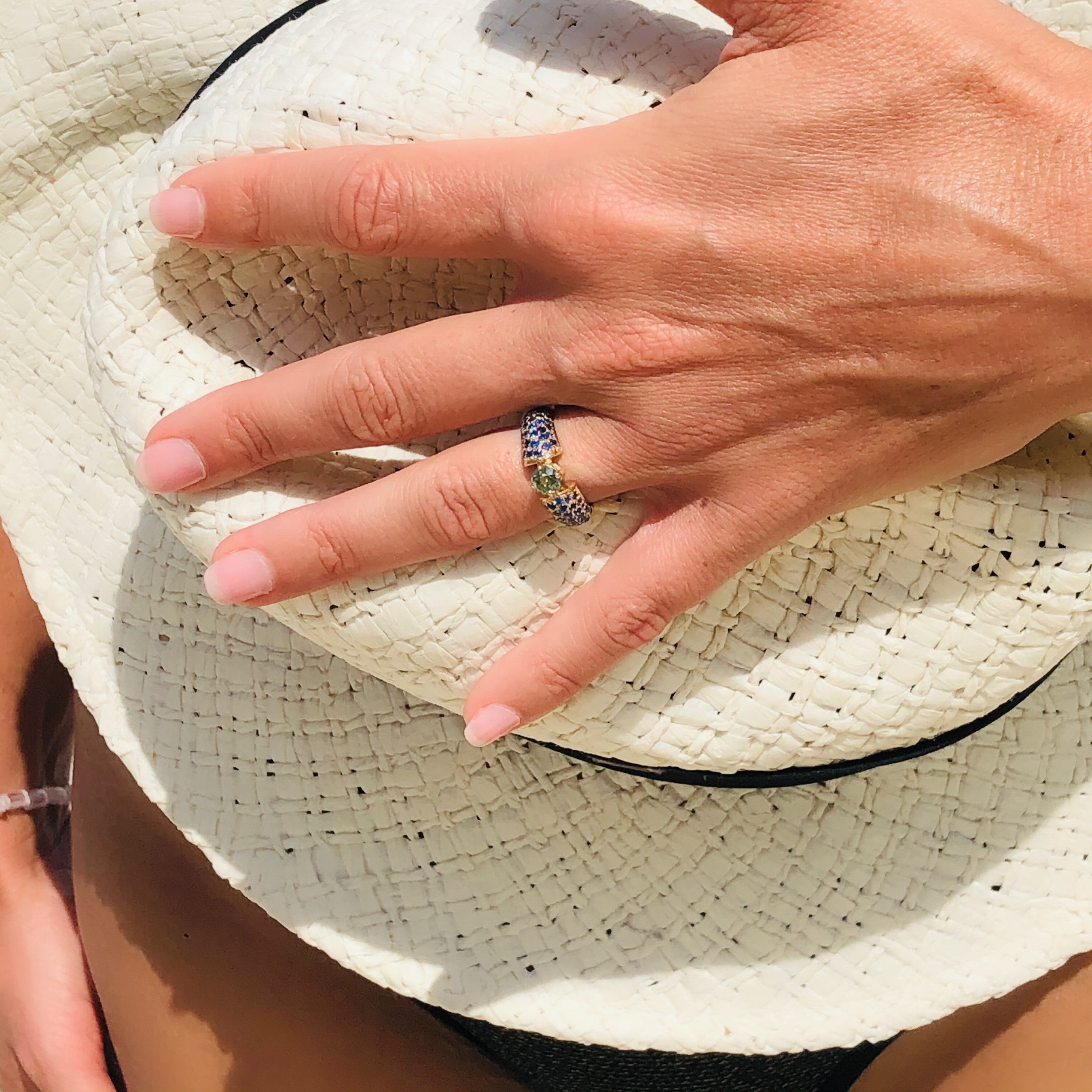 Blue and Green Sapphire Ring photographed on models ring finger. Panama hat in the background