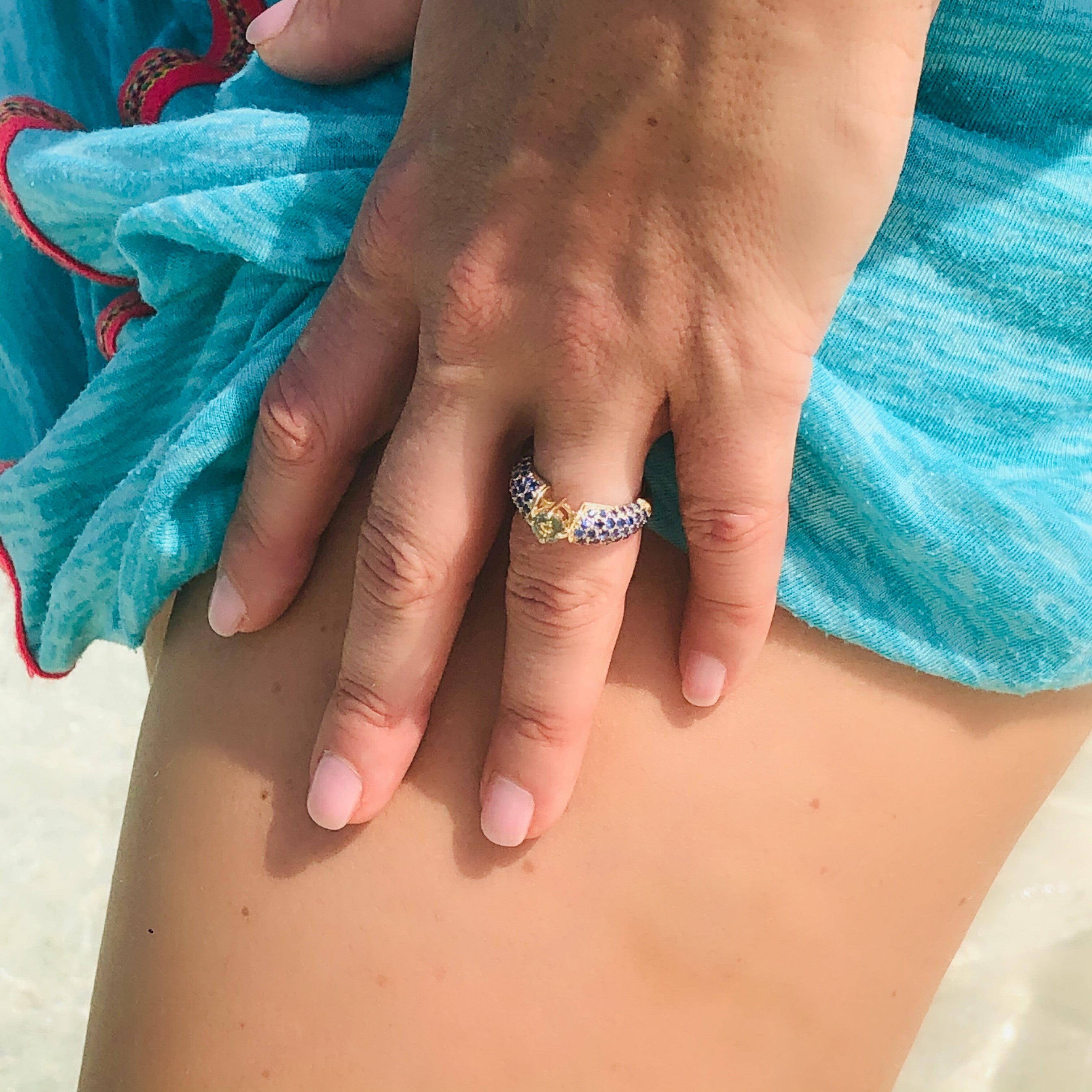 Blue and Green Sapphire Ring photographed on models ring finger. Light blue green sarong and models leg in the background.