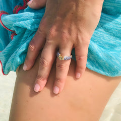Blue and Green Sapphire Ring photographed on models ring finger. Light blue green sarong and models leg in the background.
