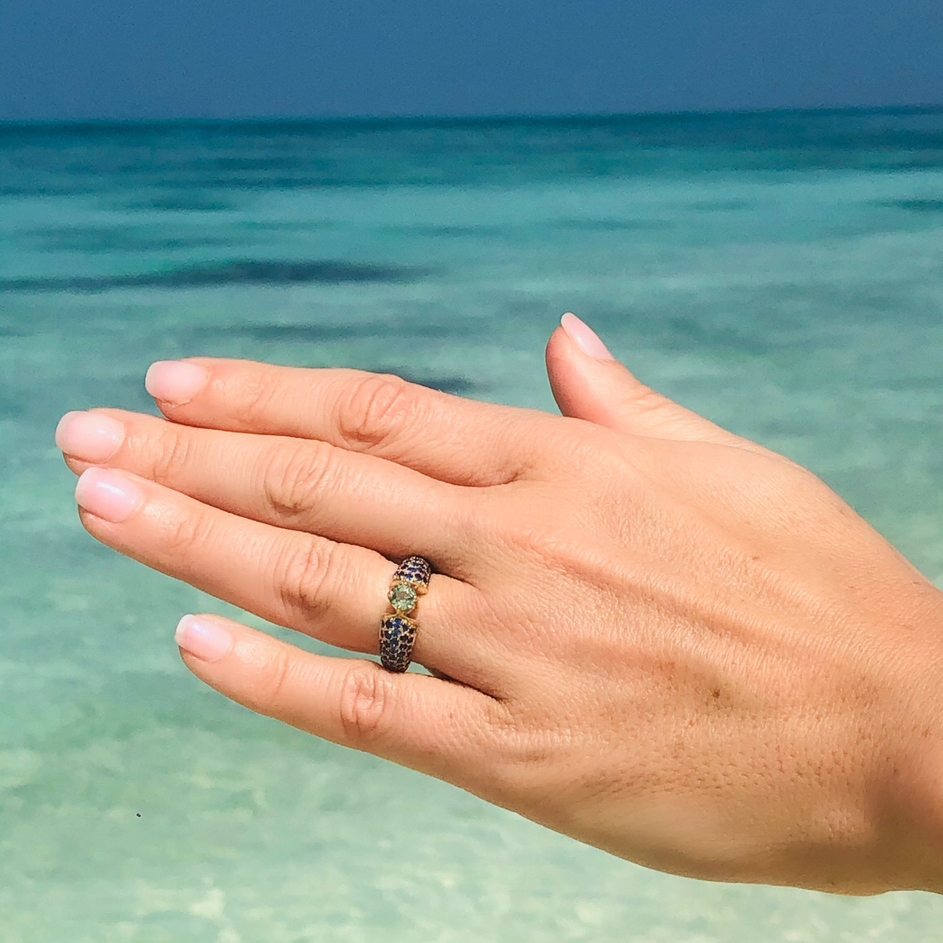 Blue and Green Sapphire Ring photographed on models ring finger. Blue ocean and sky in the background.